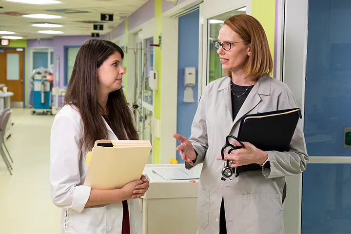 Two women in white coats talking in a hallway